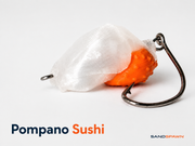 SandSpawn Pompano Sushi artificial sand flea lure in pearl and orange with hook on a white background.